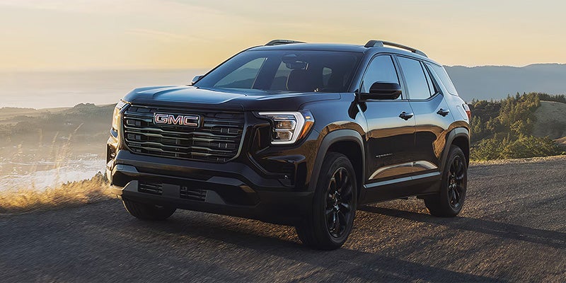 Black GMC Terrain driving on a coastal road with mountains and ocean views in the background.